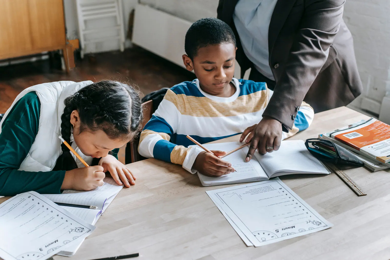 A teacher guides two elementary students as they complete mathematics assignments.