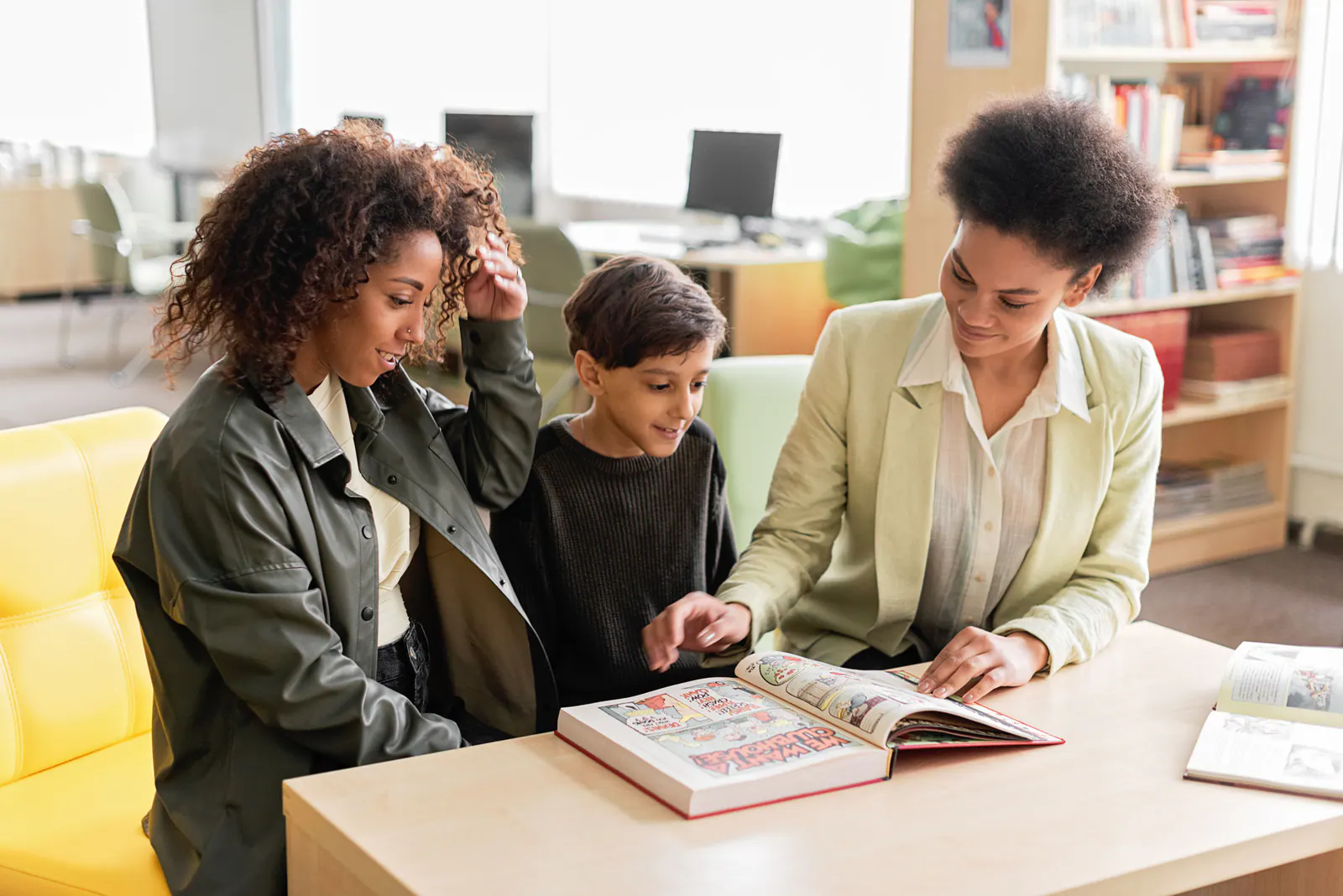 Two adults and a child reading together in a bright library.