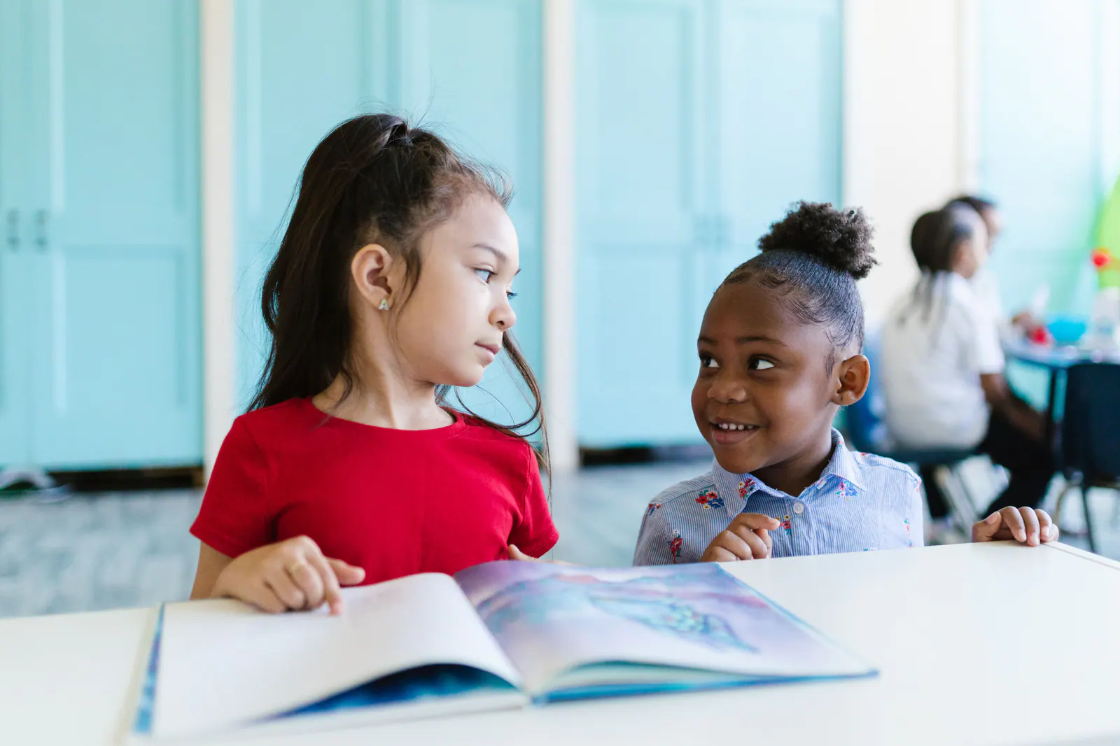 Two elementary students reading a picture book together in a classroom.